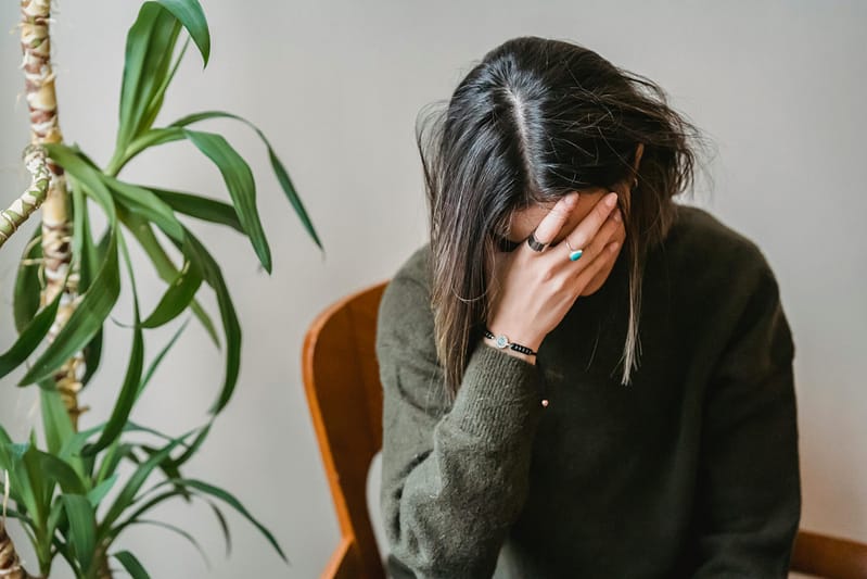 A woman sitting on a chair, held her head as if looking stressed or depressed.